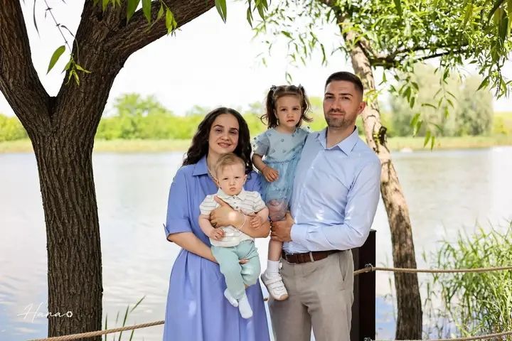 Family of four posing by a lake under trees